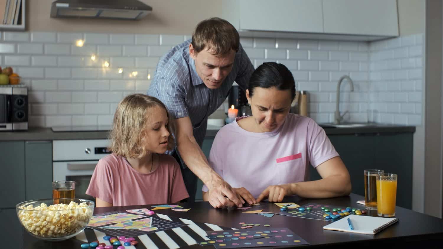 Family of three playing board games at a table in their kitchen, connecting the geometric shapes of a tangram puzzle. Family lifestyle concept