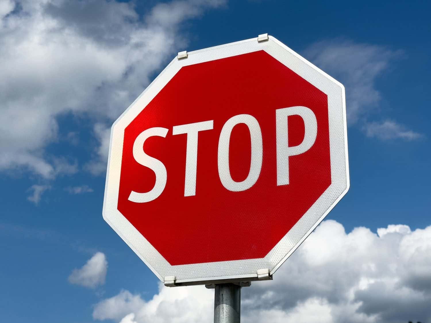 Bright red stop sign against blue sky and clouds.