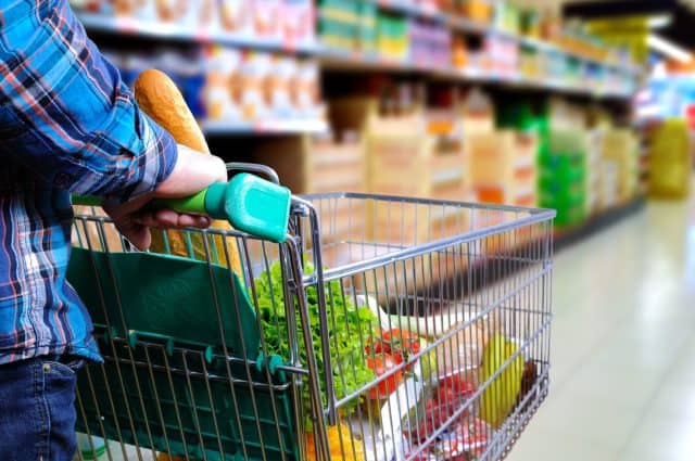 Man pushing shopping cart full of food in the supermarket aisle. Elevated rear view. horizontal composition