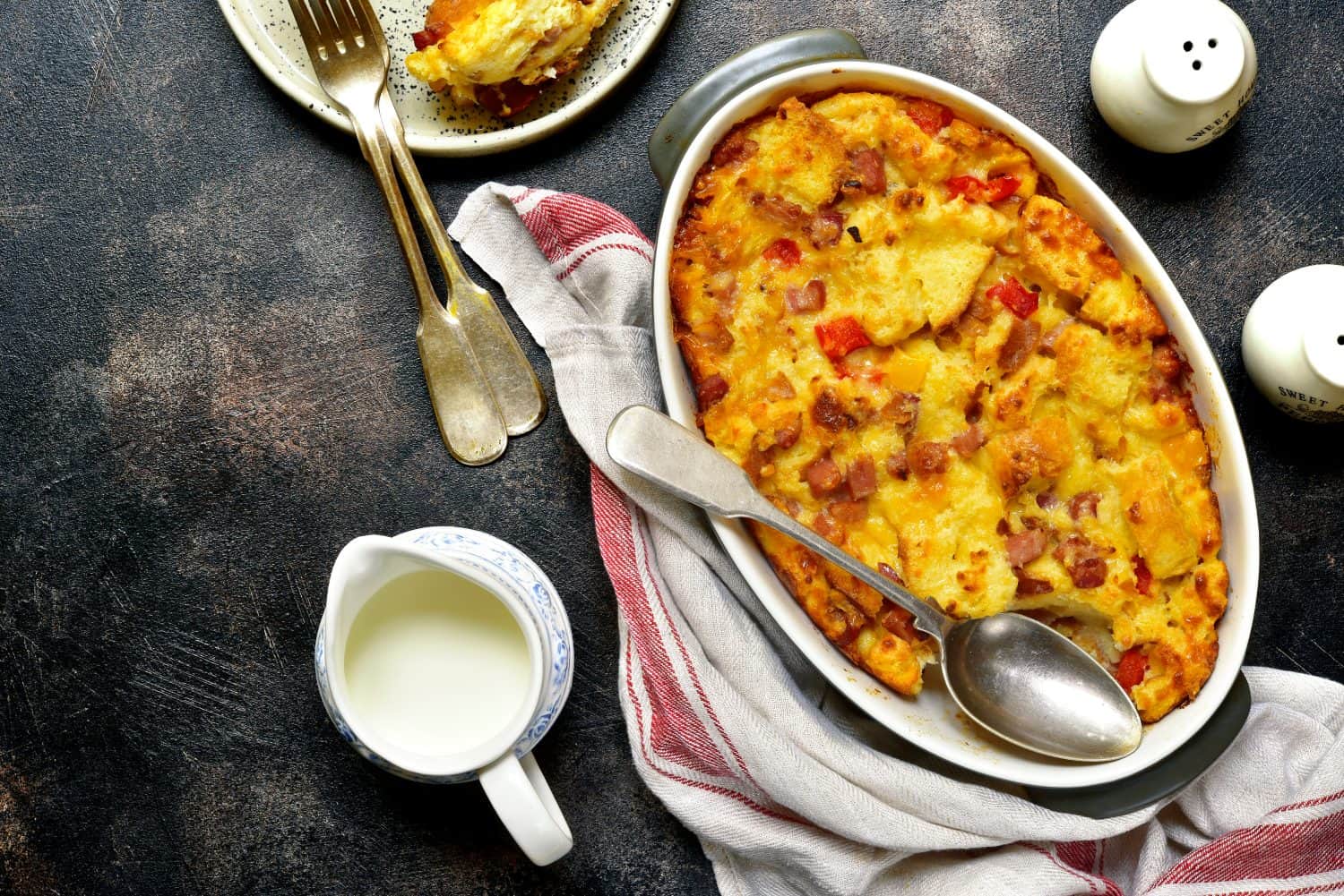 Bread pudding with bacon and cheese in a baking dish over dark slate,stone or metal background.Top view.