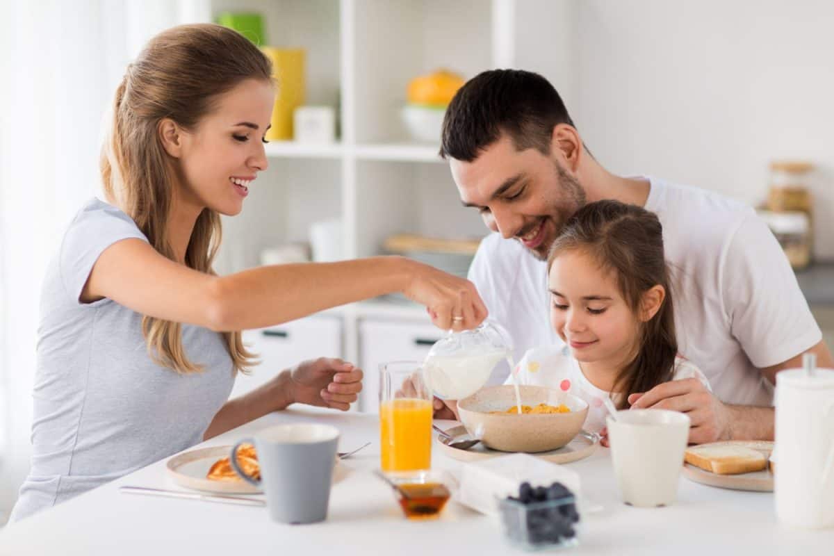 family, eating and people concept - happy mother, father and daughter having breakfast at home