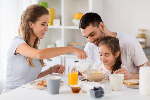 family, eating and people concept - happy mother, father and daughter having breakfast at home