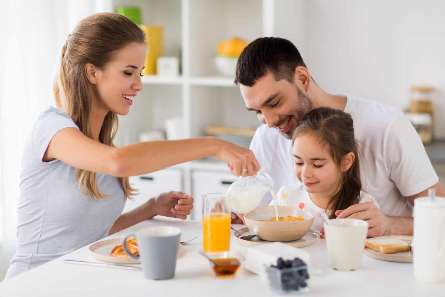 family, eating and people concept - happy mother, father and daughter having breakfast at home