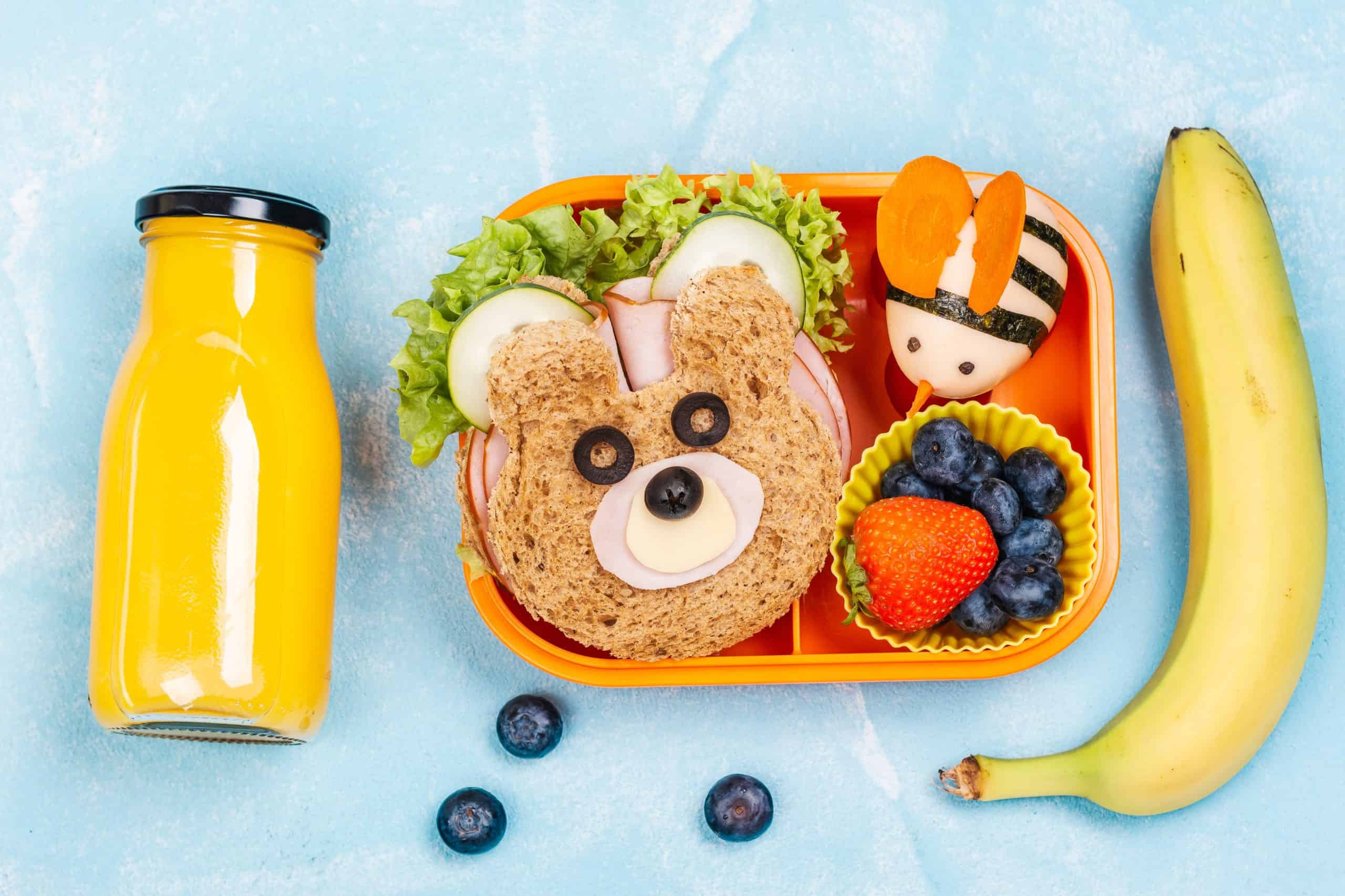 Kids lunch box with funny bear sandwich and boiled egg bee, banana, orange juice. Back to school background. Top view