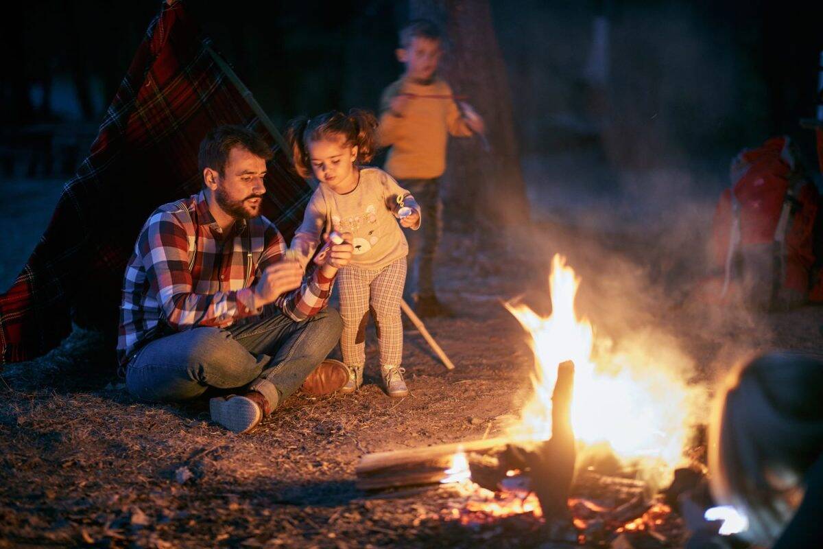 Father and children having a good time around campfire in the forest on a beautiful autumn dusk