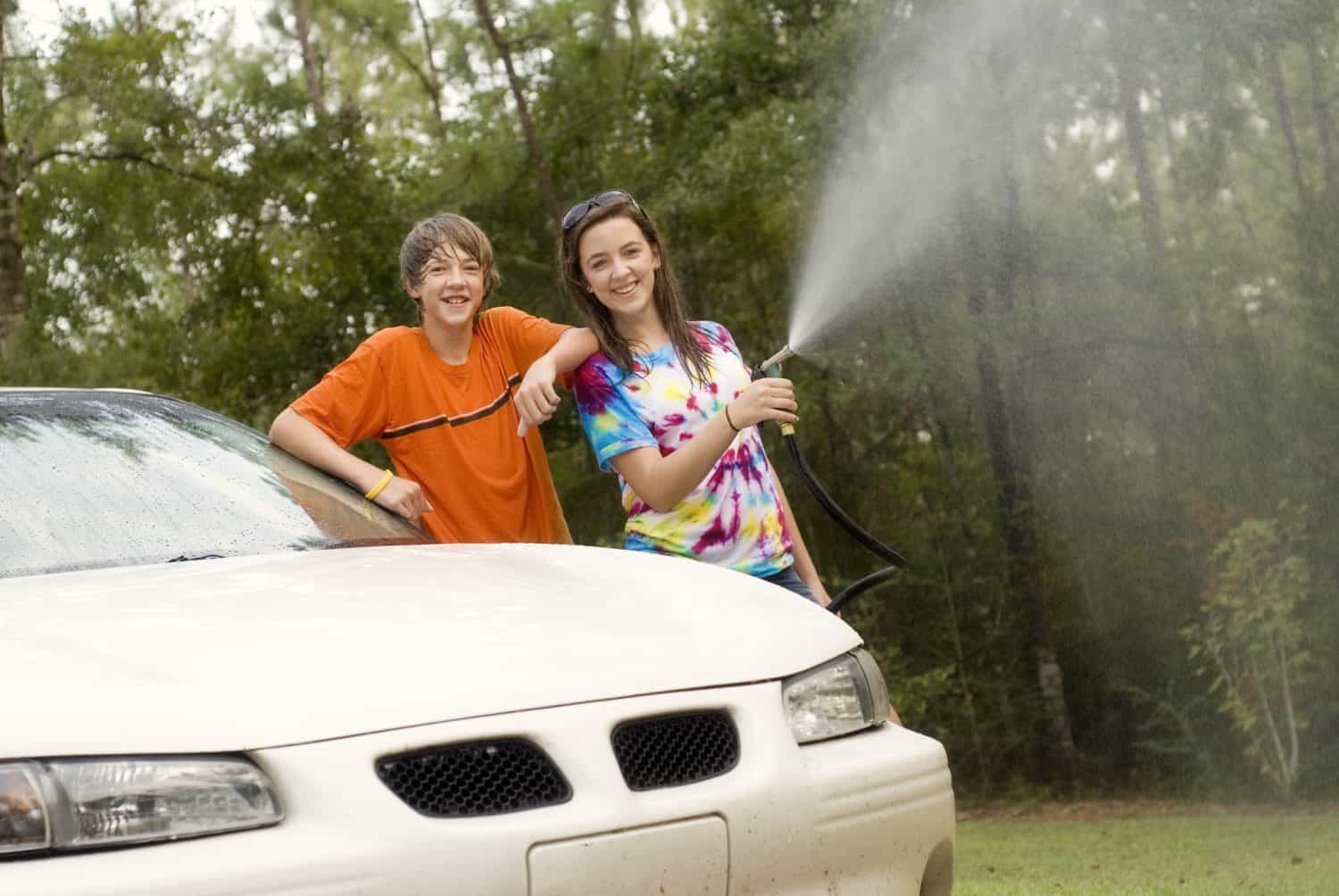 two young teens - boy and a girl - at home washing the car