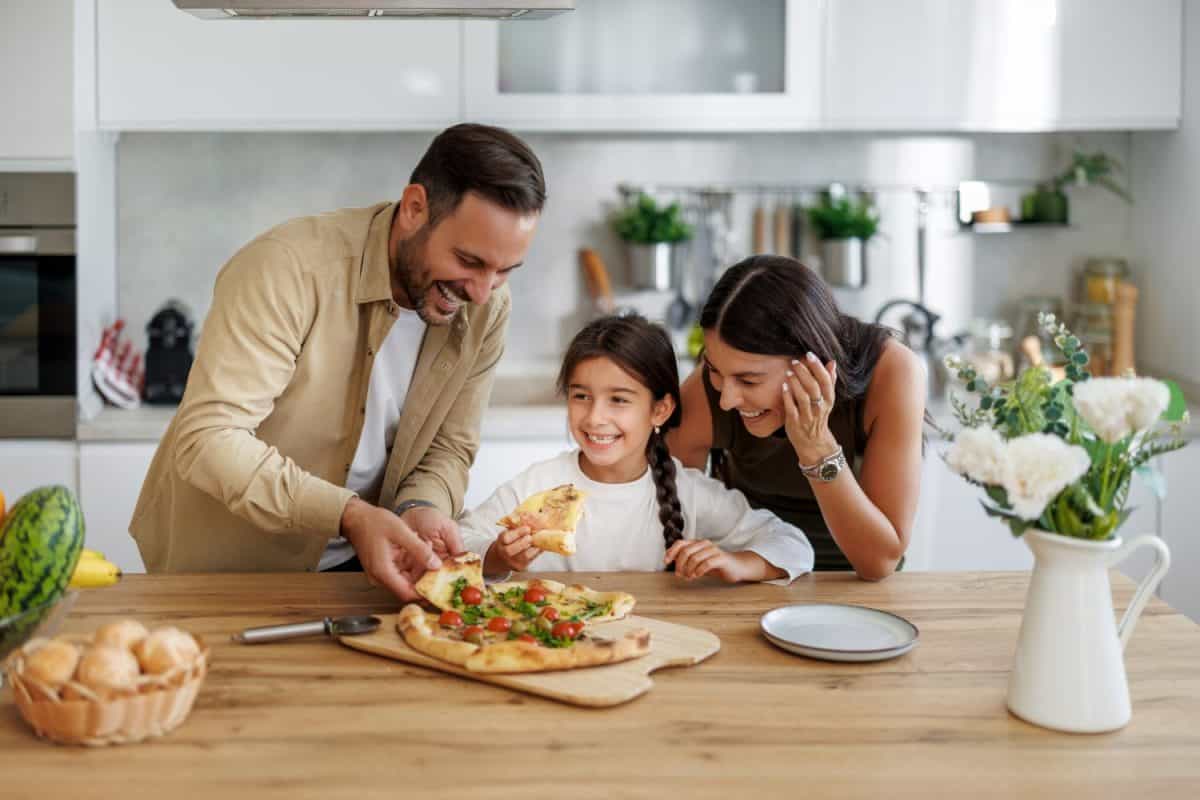 A cozy family gathers around the table at home, delighting in a delicious pizza dinner together. Laughter fills the air as they share slices, creating cherished memories.