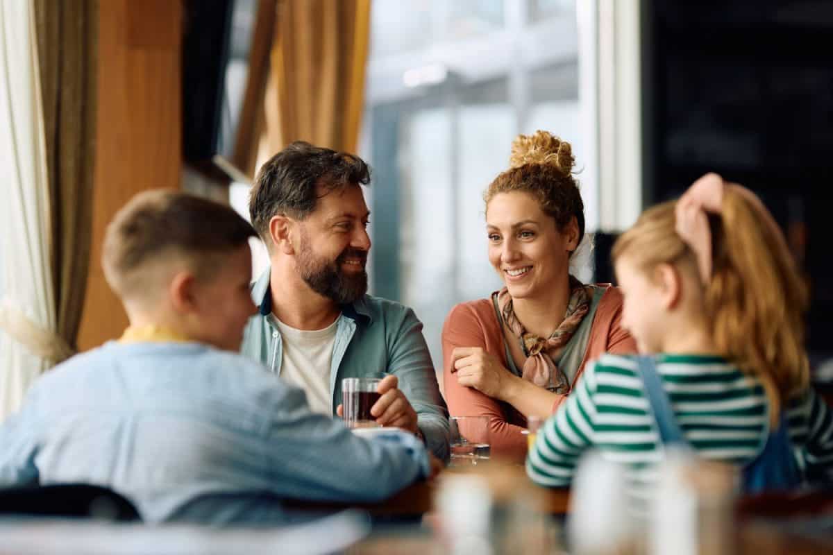 Happy parents communicating with their children while having a meal in a restaurant.