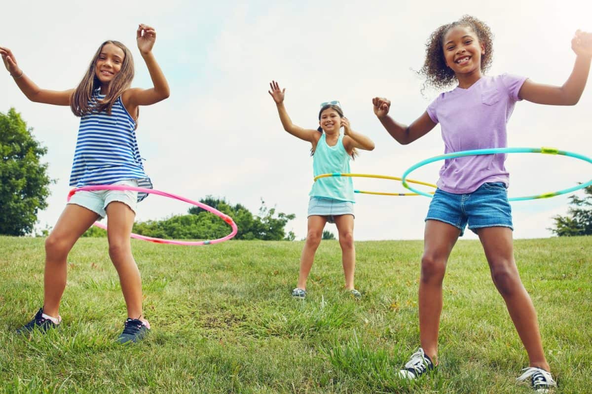 Portrait, hula hoop and children in park, girls and happiness with fun, bonding together and playful. Leisure, outdoor or friends with recreation, game or cheerful with weekend break, summer or smile