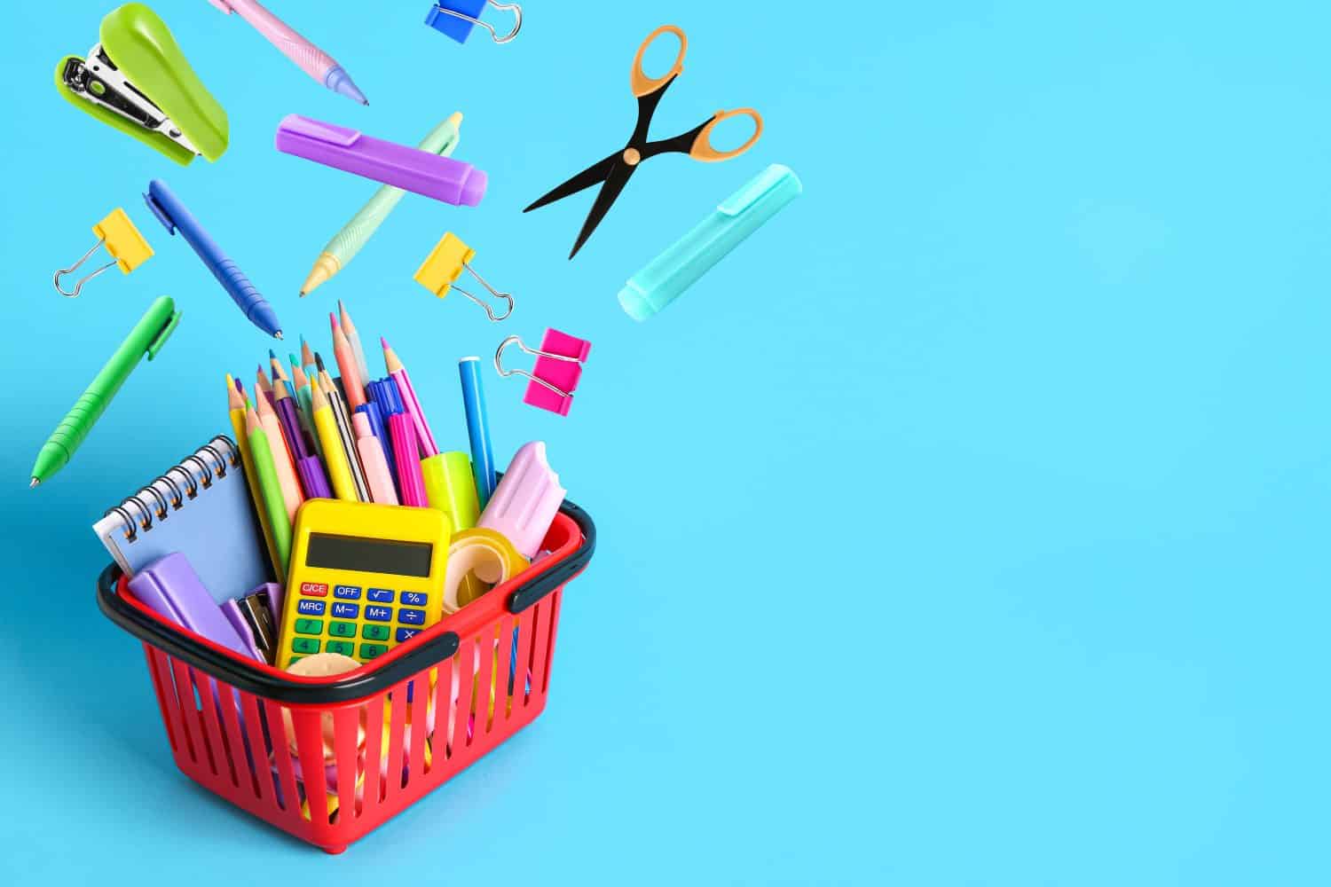 Shopping cart and different flying school stationery on light blue background
