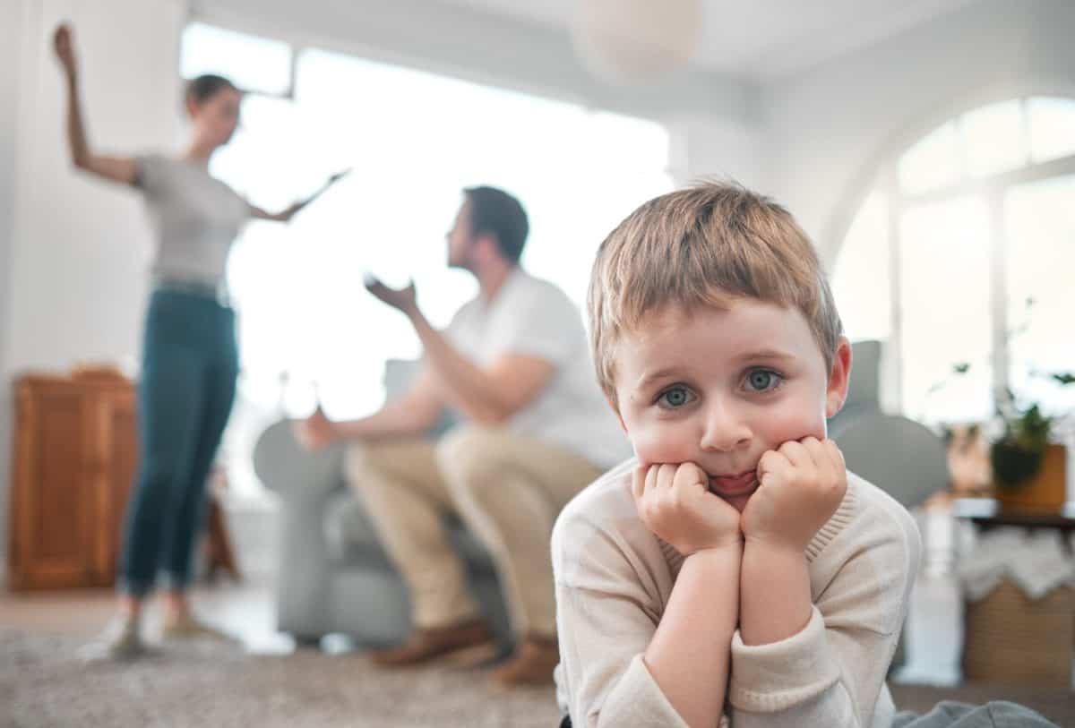 Sad, child and parents fighting in home for infidelity, cheating or affair in marriage with divorce. Upset, portrait and boy kid in living room with mother and father in argument for family drama.
