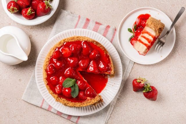 Table with homemade dessert. Classic baked Cheesecake with a strawberry topping sauce directly above.
