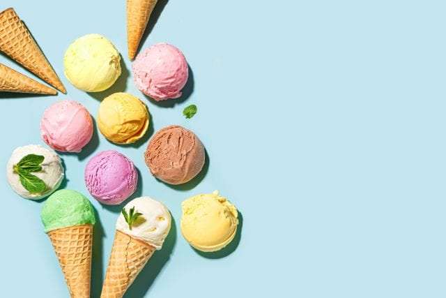 Assorted scoops of ice cream on blue background, top view, copy space. Various ice creams or gelato with waffle cones, healthy summer dessert creative concept.