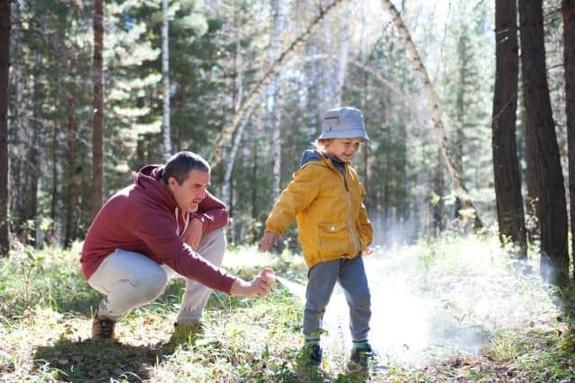 Father spraying insect repellents on his son before a walk in the forest
