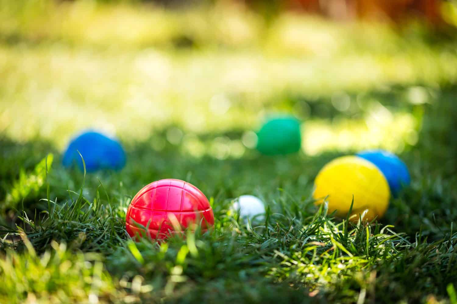 a lot of colorful plastic boules or boccia balls are lying on a green meadow in the summer
