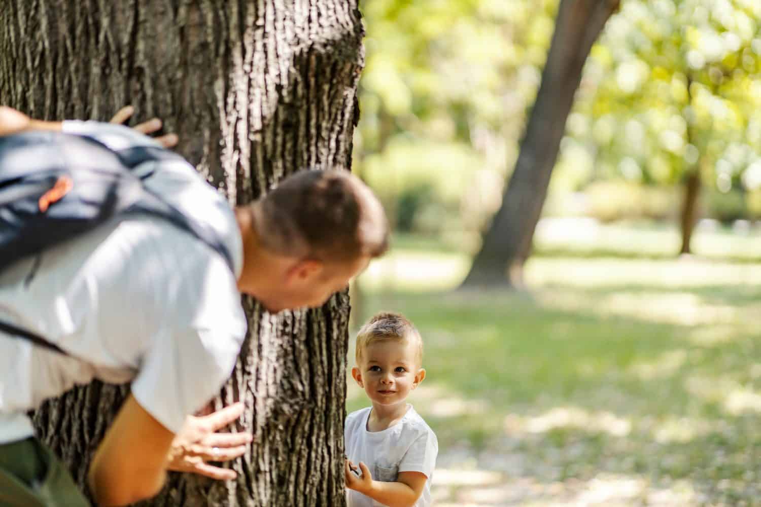 A son playing seek and hide with his father in woods.