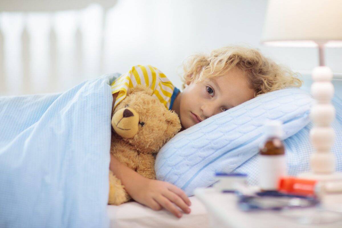 Sick little boy with asthma medicine. Ill child lying in bed. Unwell kid with chamber inhaler for cough treatment. Flu season. Bedroom or hospital room for young patient. Healthcare and medication.
