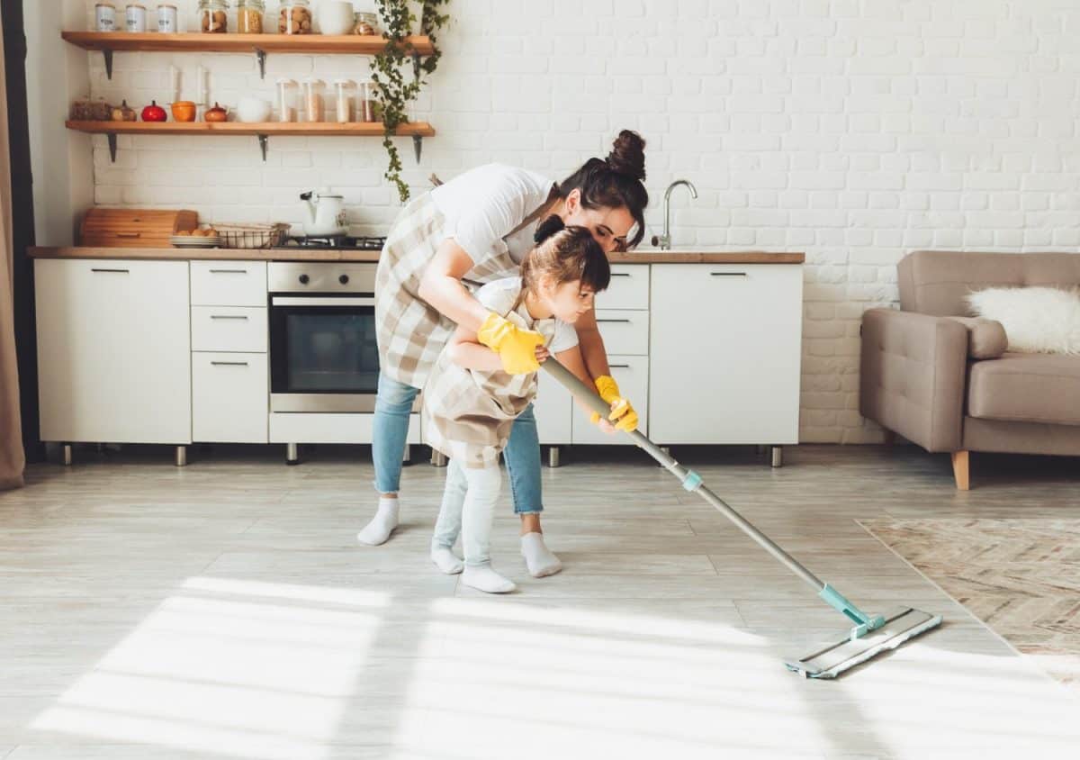 a little daughter and her mom clean the house, a child washes the kitchen floor, a cute little helper girl cleans the floor with a mop, a happy family cleans the room.
