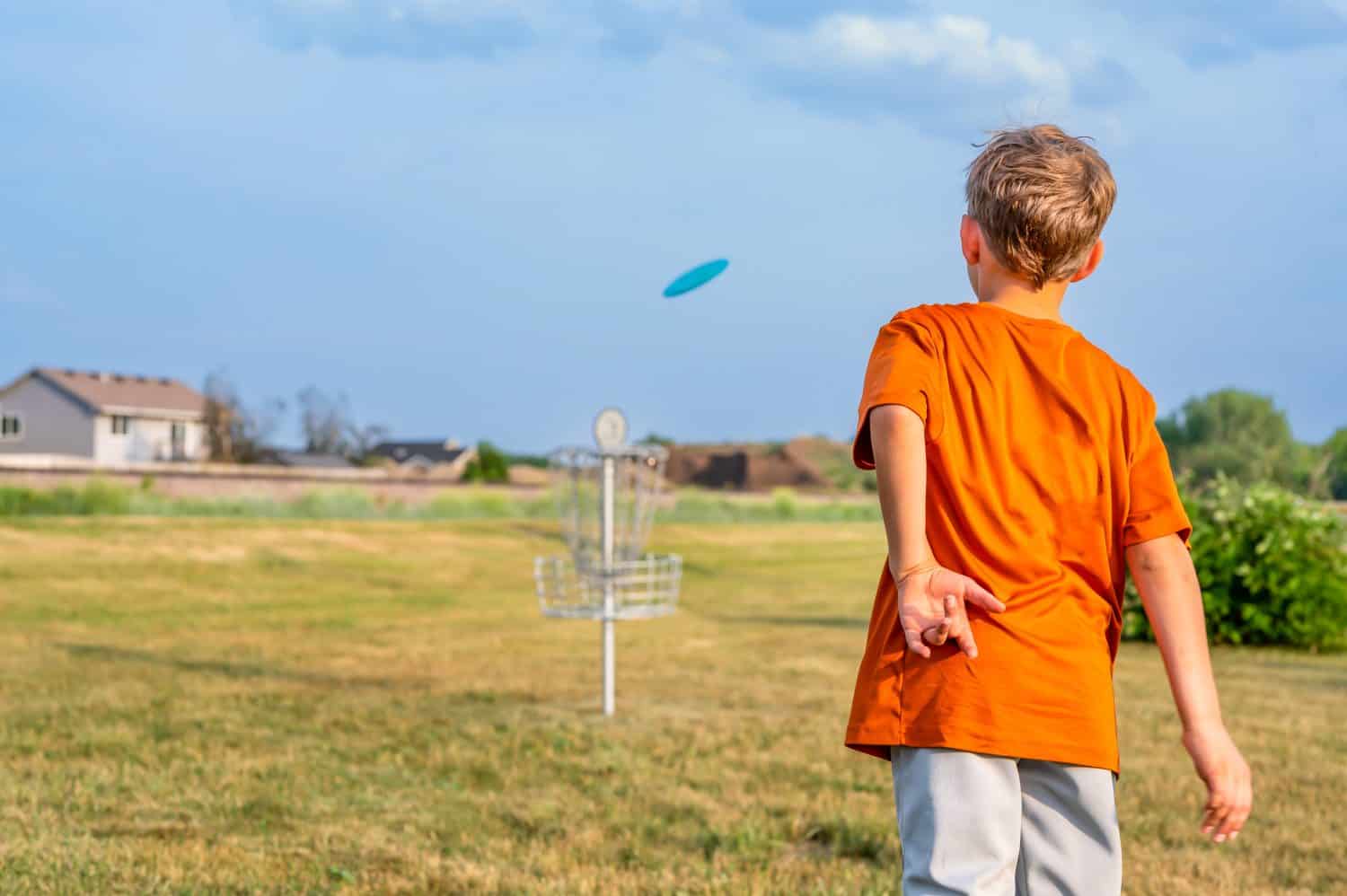 Young Caucasian male boy aiming a disc golf at a chain goal. 