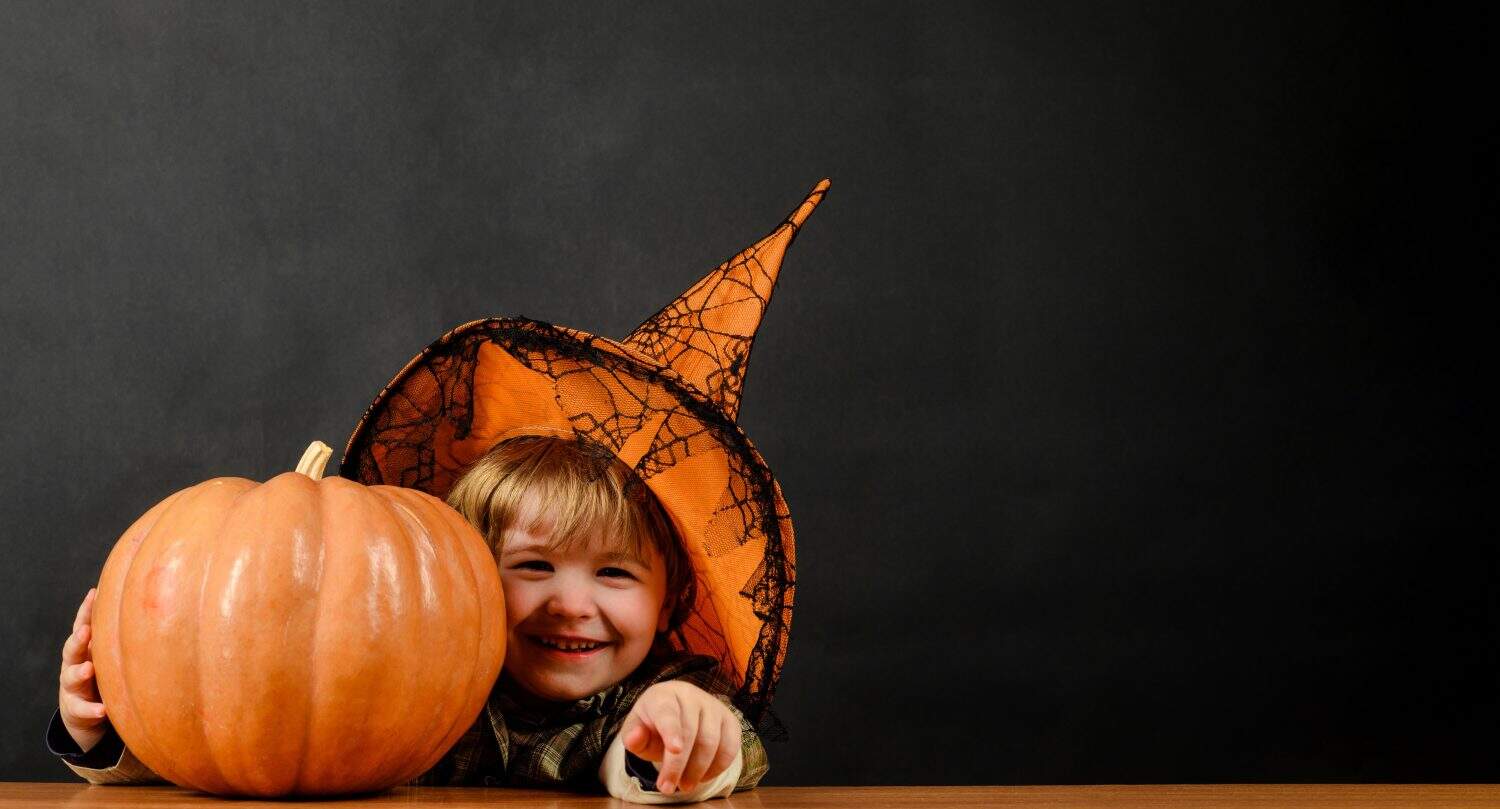 Halloween child with jack-o-lantern pumpkin. Smiling kid in witch hat with Halloween pumpkin. Preparation for Halloween holiday. Trick or treat. Halloween sale. Discount. Copy space for advertising