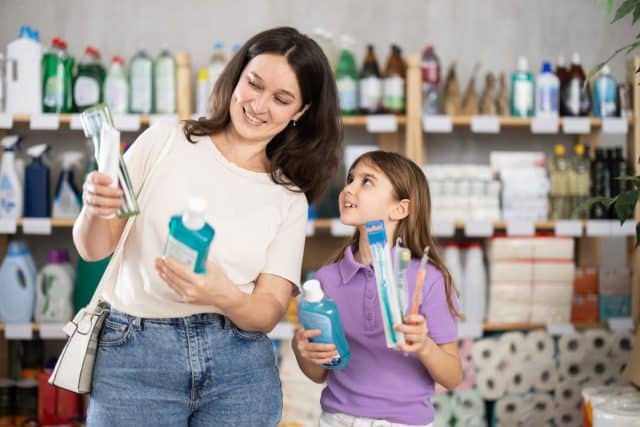Adult woman and her daughter buyers choosing dental care products in household chemicals store