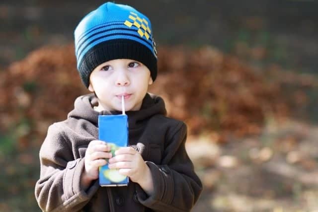 European two years old boy drinks juice and dreaming at the park