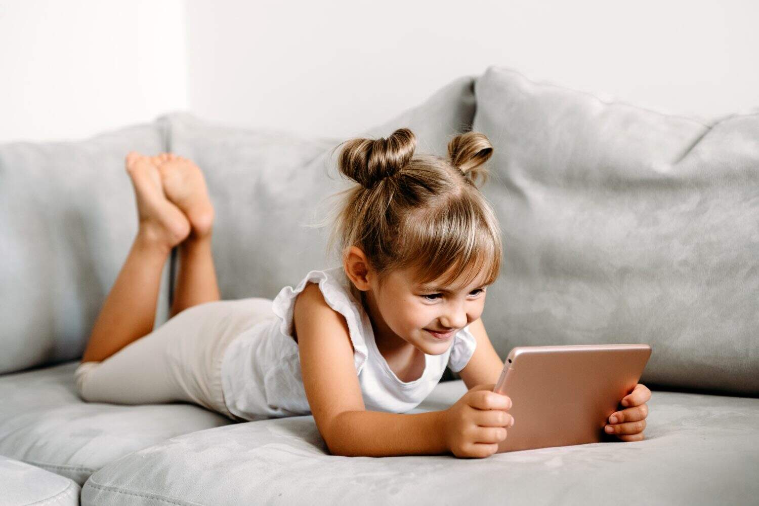 Toddler girl playing with digital wireless tablet computer on couch at home. Baby child growing with online applications. Child and electronic devices concept. Portrait of toddler with smartphone.