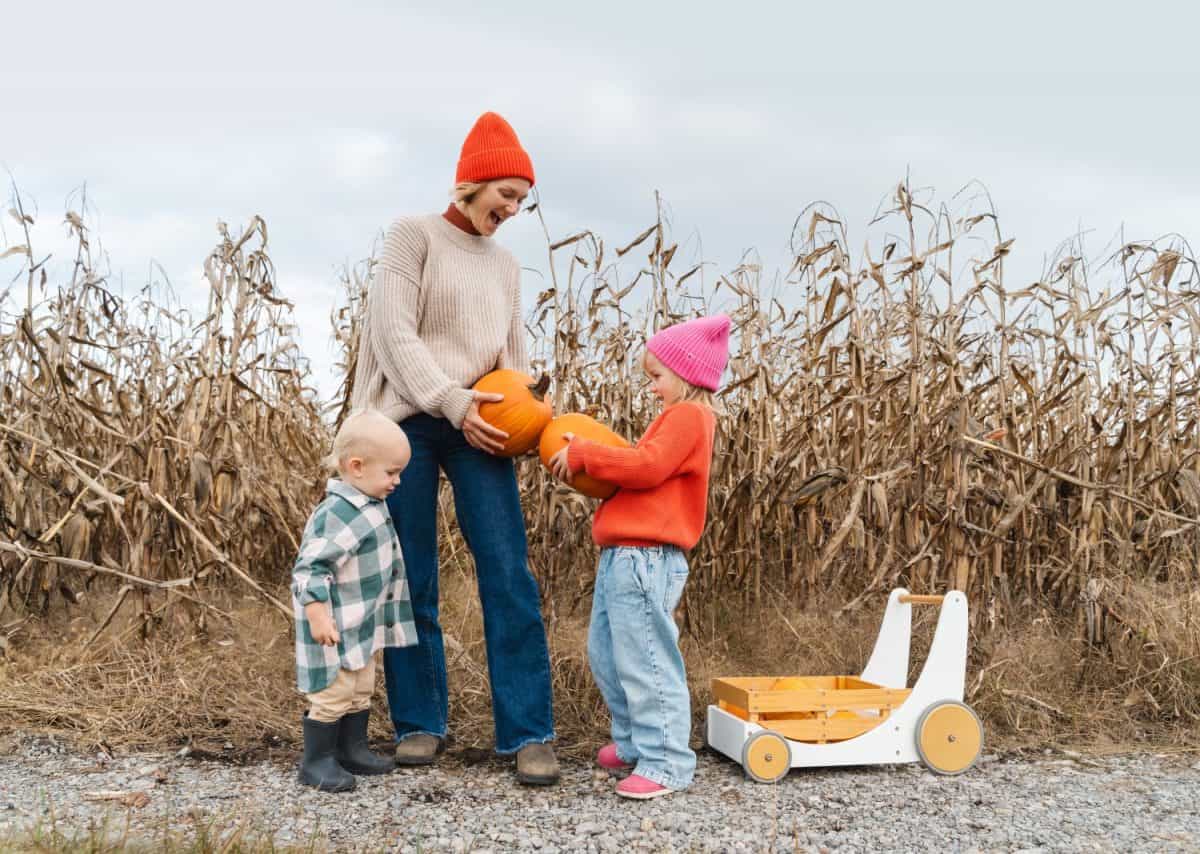 Mother with little children playing together in pumpkin patch. Mom with son and daughter picking pumpkins against of field in autumn. Family fun Thanksgiving traditions and Halloween.