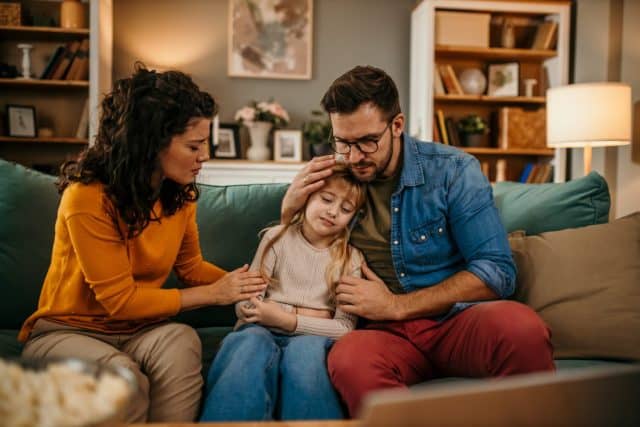 Sad little girl at home being consoled by her parents