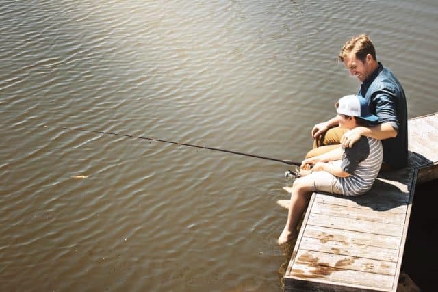 Fishing, lake and father with son in nature for teaching skill, adventure and vacation together outdoors. Family, happy and dad with young boy by river with rod for sports, hobby and catch fish