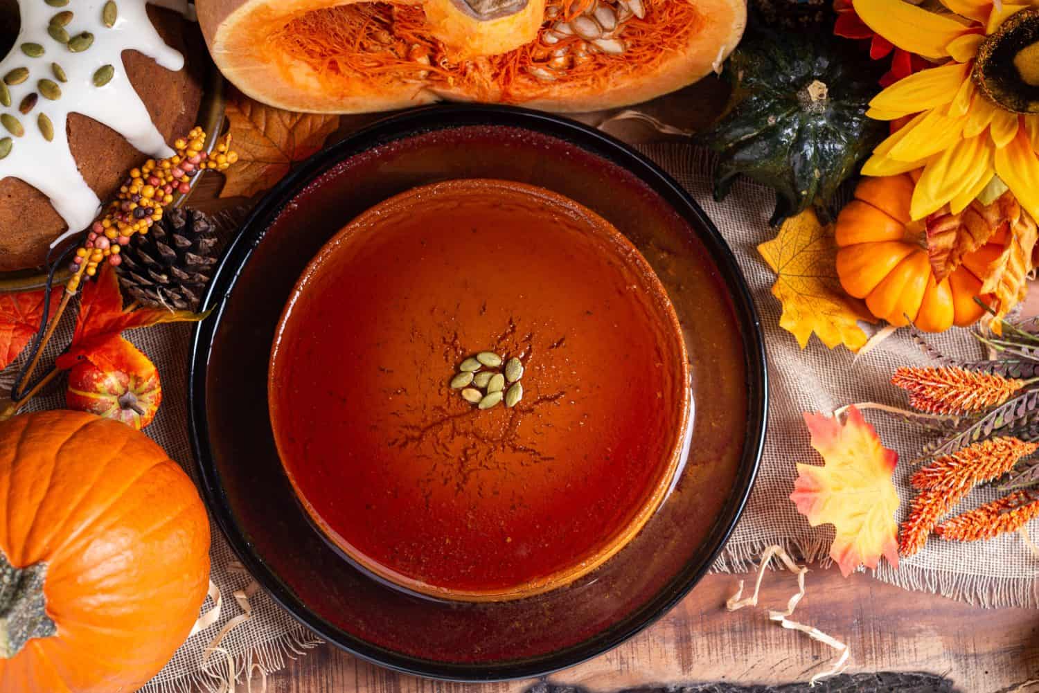 A glistening pumpkin flan, adorned with pumpkin seeds, sits on a dark plate.