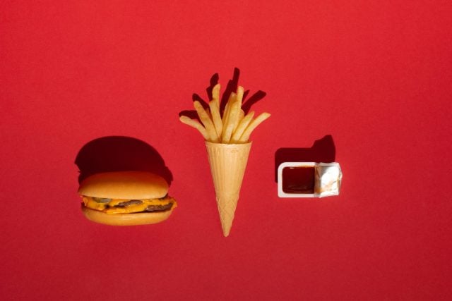 McDonald's menu: French fries in a cup and burger on red background. Minimal concept