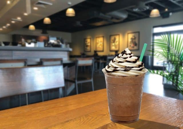 Frappuccino with cream and chocolate sauce in takeaway cup on wooden table
