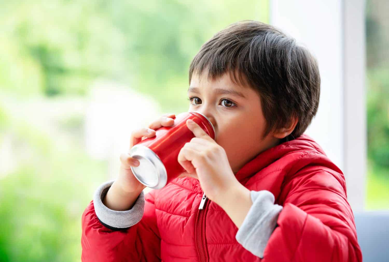 Close up side view of cute little boy drinking soda, Kid boy looking out of window with thinking of something while drinking soft drink, Unhealthy food and drink for Children concept