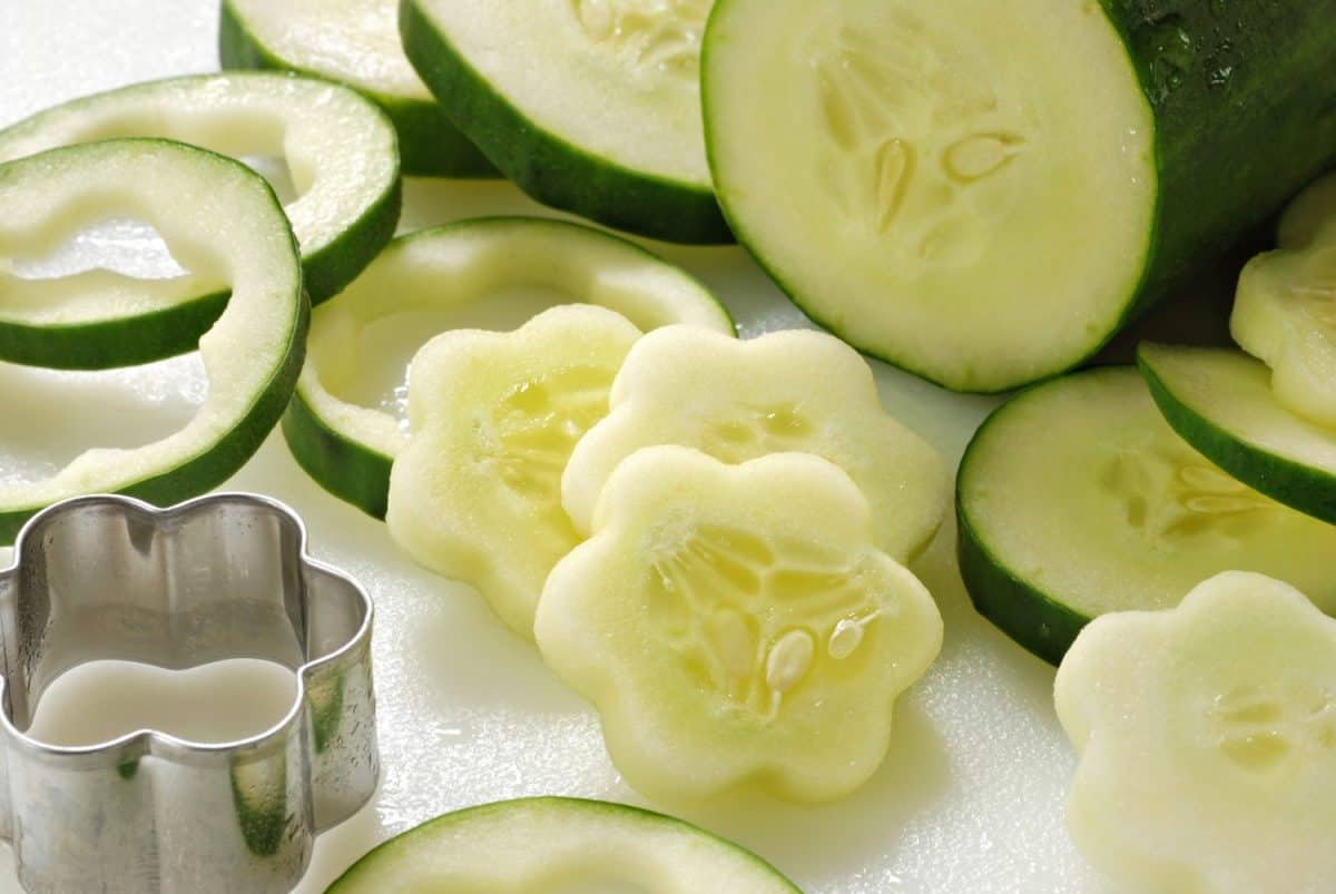 Freshly sliced cucumbers being cut into flower shapes (with mini cookie cutter) on white cutting board. Closeup with shallow dof.