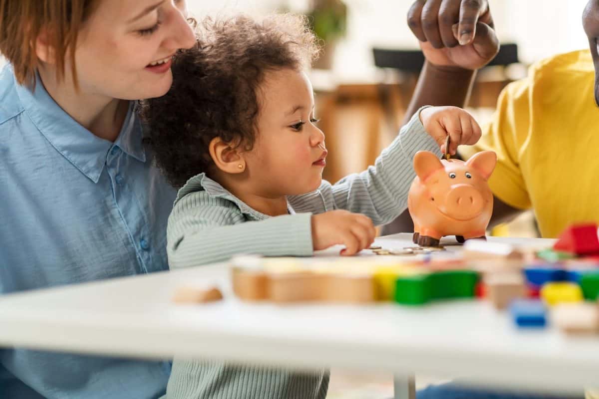 A child is putting a coin into a piggy- bank. Savings bank accounts for kids concept. Child saving money for future - concepts. Multi-ethnic family