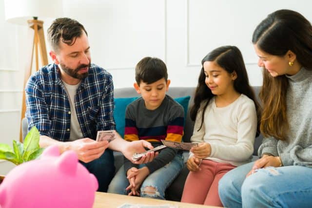 Happy parents giving allowance money to their little kids and teaching about savings and financial education