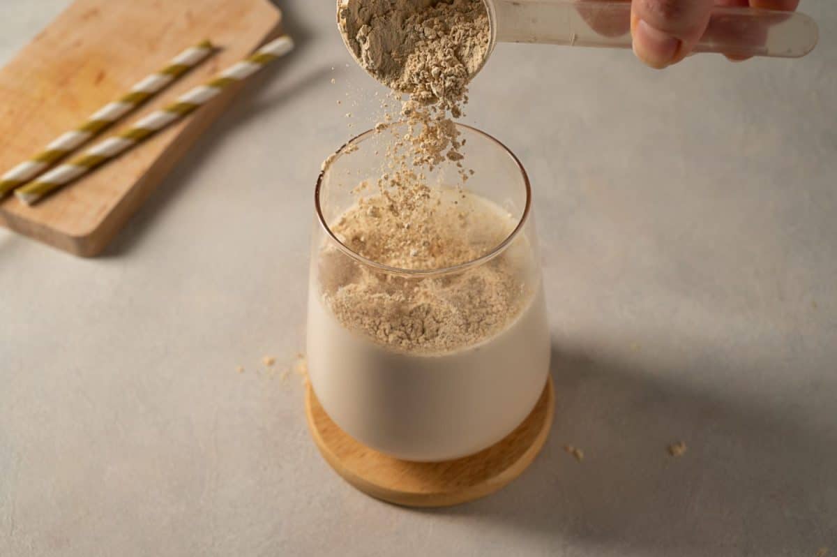 Pouring protein powder from scoop, in glass with milkshake.