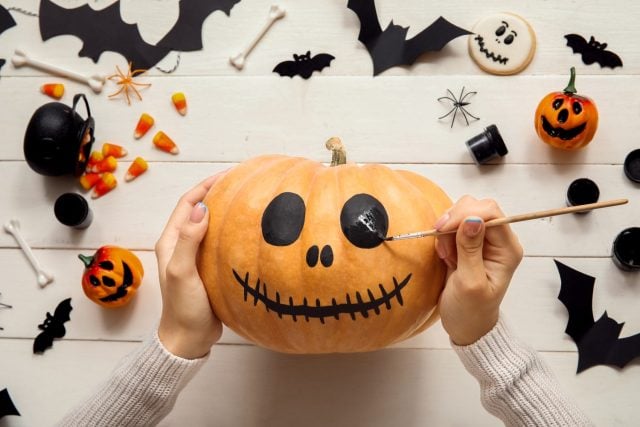 Woman painting Halloween pumpkin at white wooden table
