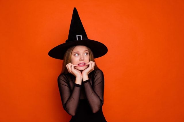 Photo portrait of lovely blonde teen lady terrified look empty space dressed black halloween garment isolated on orange color background