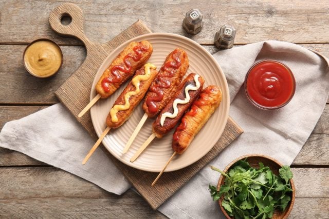 Plate of tasty corn dogs with different sauces on wooden background