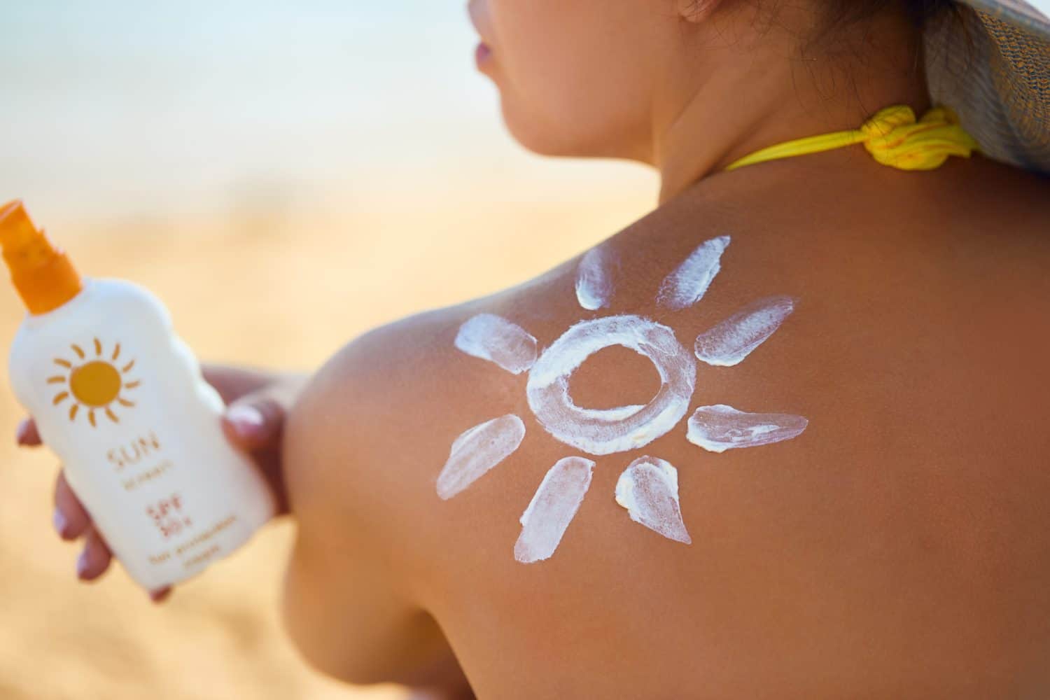 Skin care. Sun protection. Woman apply sun cream. Woman With Suntan Lotion On Beach In Form Of The Sun. Portrait Of Female With Drawn Sun On A Shoulder. Suncream. Girl Holding Moisturizing Sunblock.