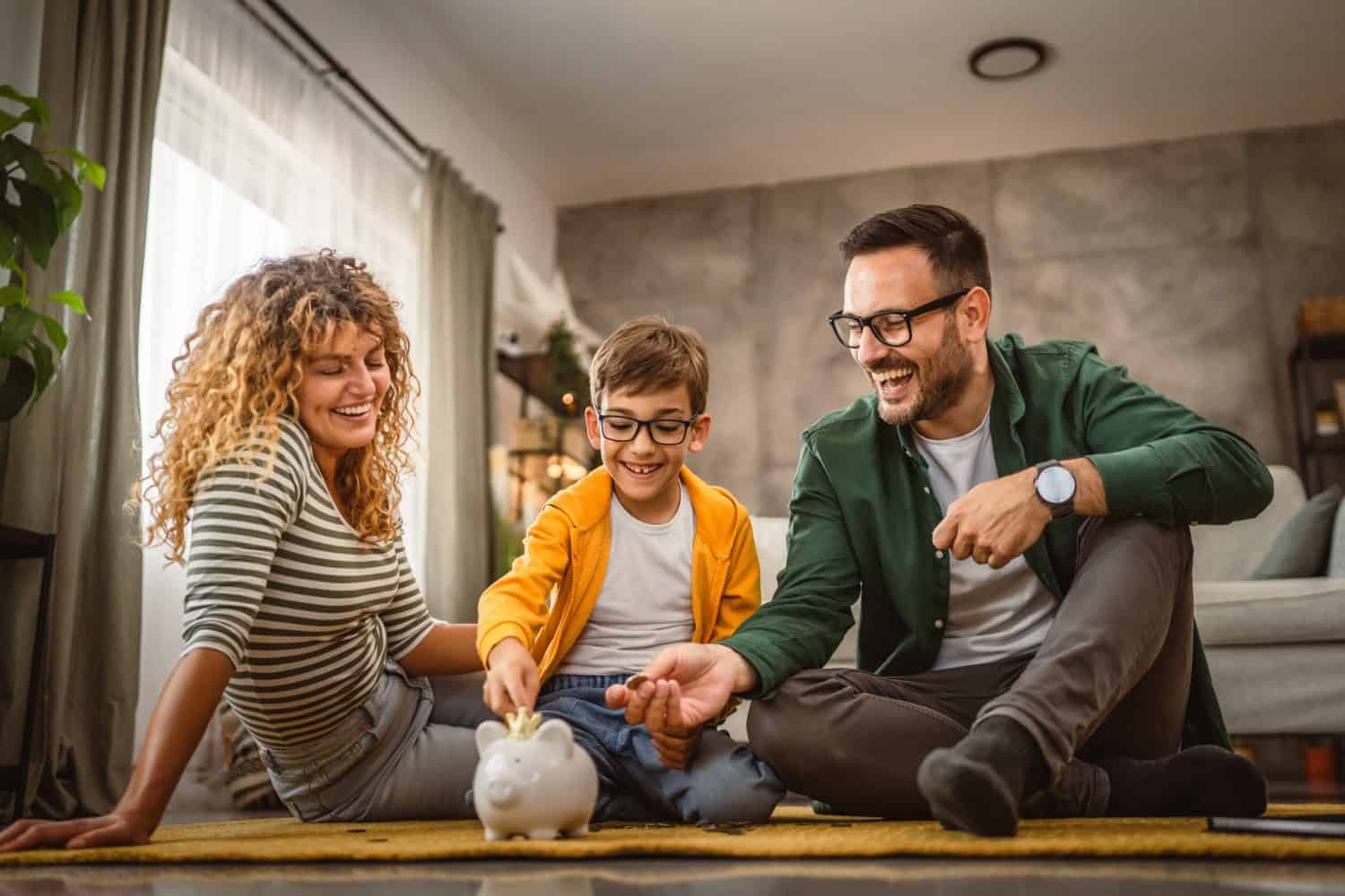 mam dad and son sit on the carpet,floor and save money in the piggy bank at home
