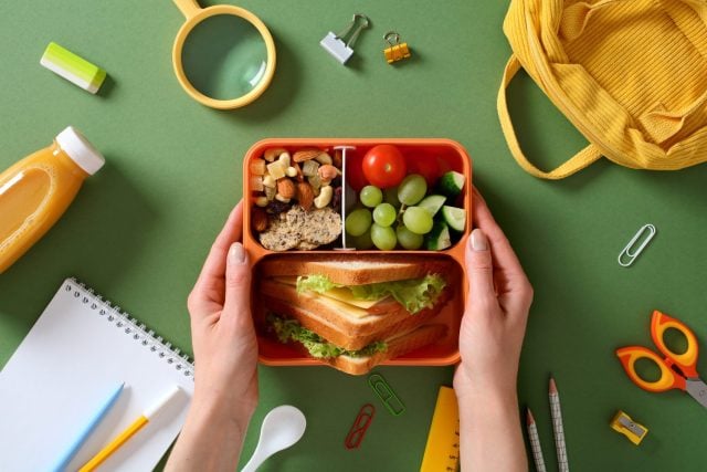 Healthy school lunch box: nutritious meal with sandwich, fruits, and nuts for kids.
