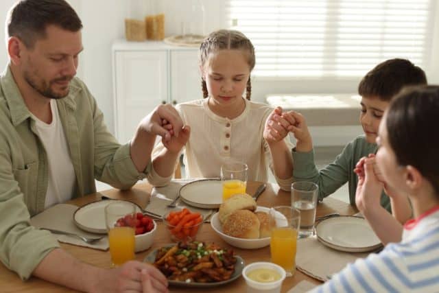 Family praying together before dinner at table indoors
