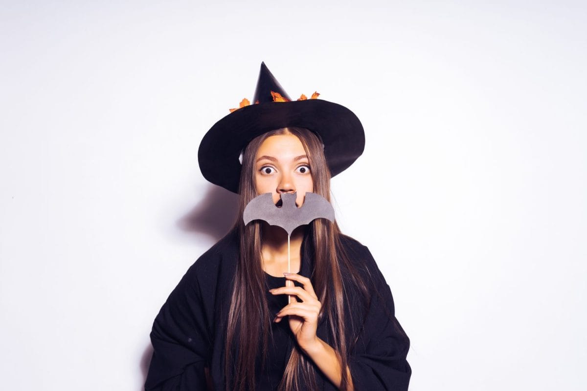 a young surprised girl dressed as a witch for Halloween, holding an artificial bat