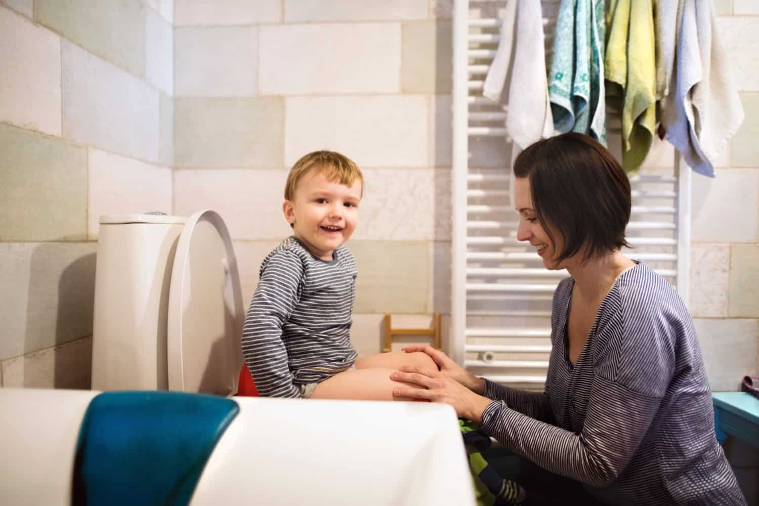 Mom is helping toddler boy use the toilet. Potty-trained little boy in the bathroom.