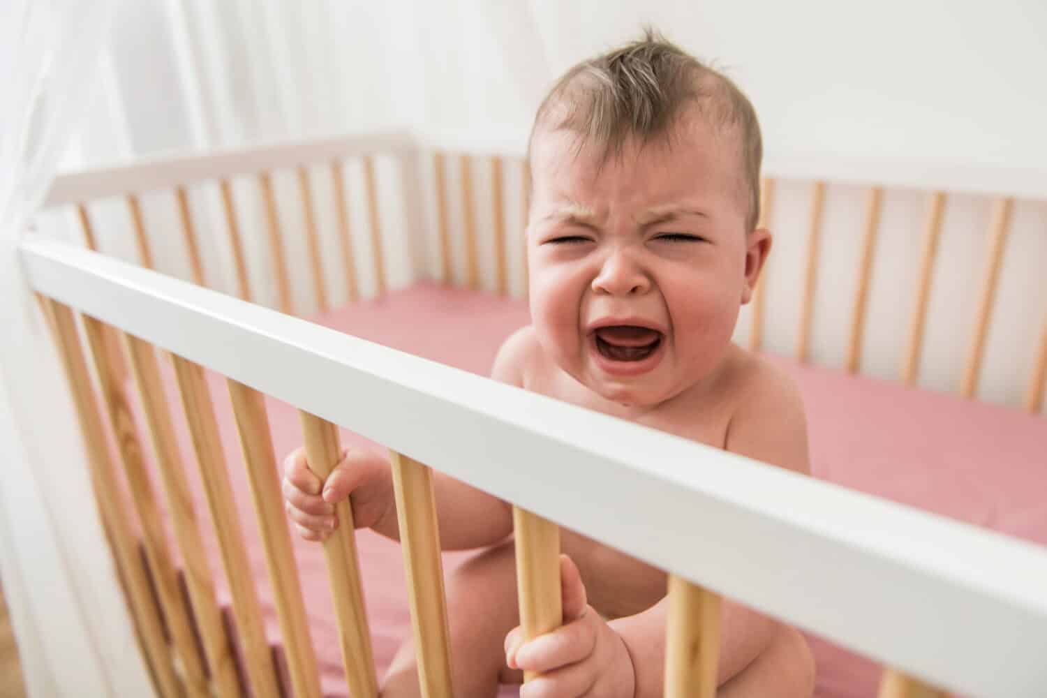 The cute baby cries and calls mum from a bed