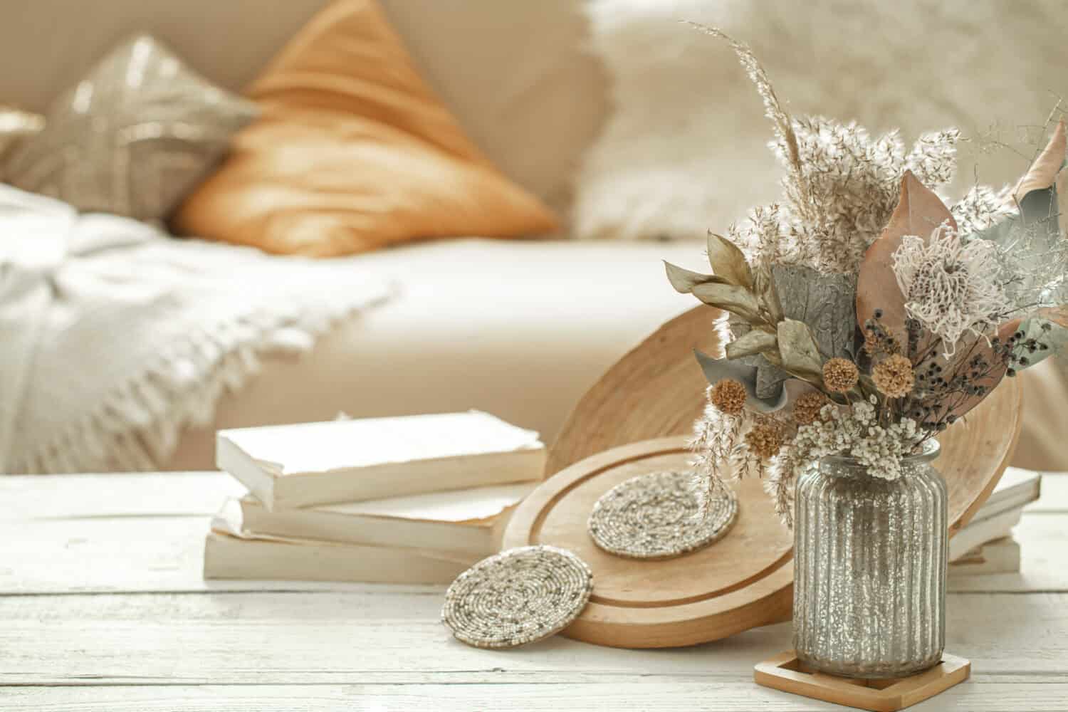 Decorative items in the cozy interior of the room , a vase with dried flowers on a light wooden table.