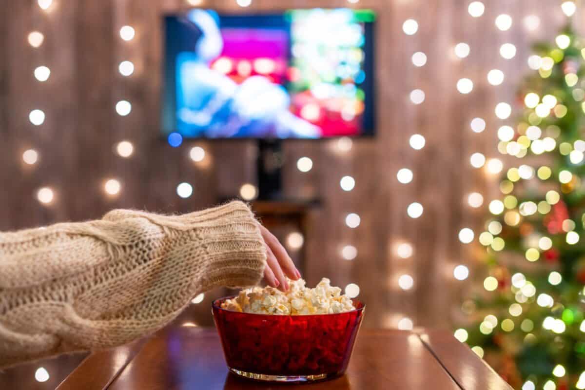 Christmas eve. Alone woman watching tv and eating popcorn. Home cinema. Cropped, close up